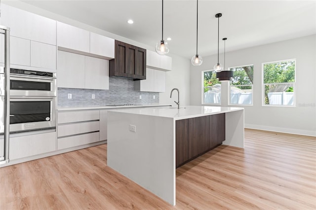 kitchen with decorative light fixtures, a center island with sink, light wood-type flooring, and dark brown cabinetry