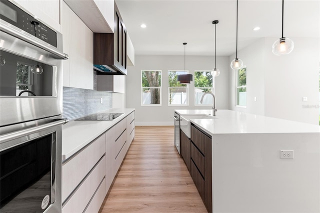 kitchen with a center island with sink, double oven, light wood-type flooring, and dark brown cabinets