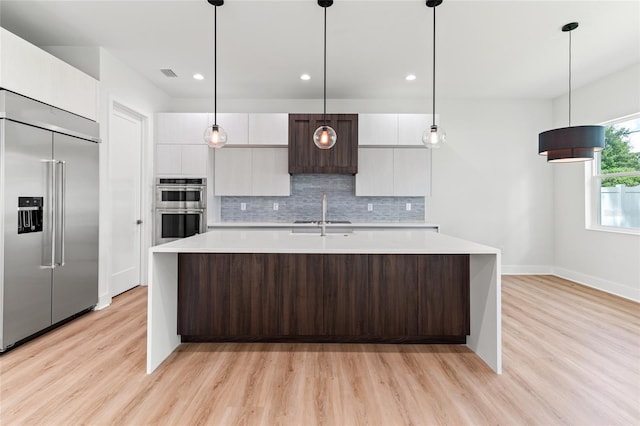 kitchen featuring light hardwood / wood-style floors, stainless steel appliances, dark brown cabinetry, decorative light fixtures, and tasteful backsplash