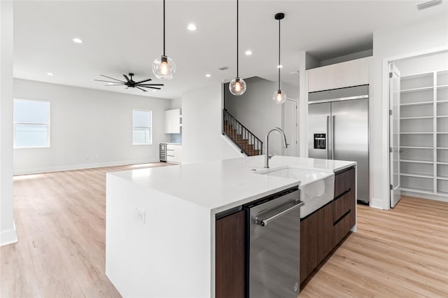 kitchen featuring stainless steel appliances, an island with sink, ceiling fan, dark brown cabinetry, and sink