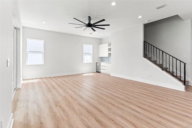 unfurnished living room with light hardwood / wood-style floors, ceiling fan, a healthy amount of sunlight, and wine cooler