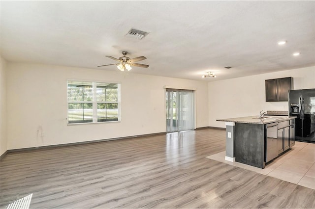 kitchen featuring light hardwood / wood-style flooring, black fridge, ceiling fan, a center island with sink, and stainless steel dishwasher