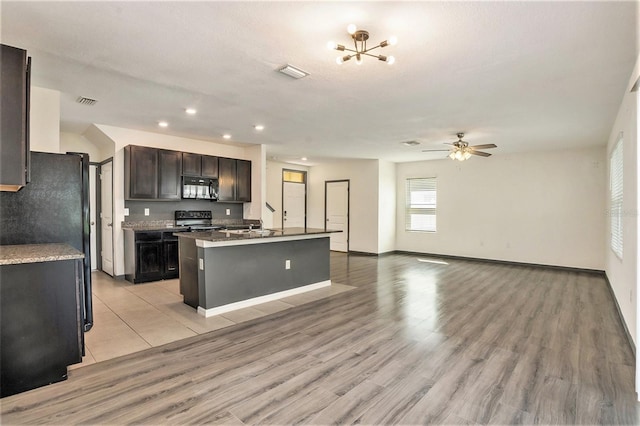 kitchen featuring ceiling fan with notable chandelier, black appliances, an island with sink, and light hardwood / wood-style floors