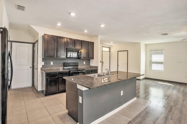 kitchen with dark brown cabinets, stainless steel appliances, an island with sink, sink, and light hardwood / wood-style floors