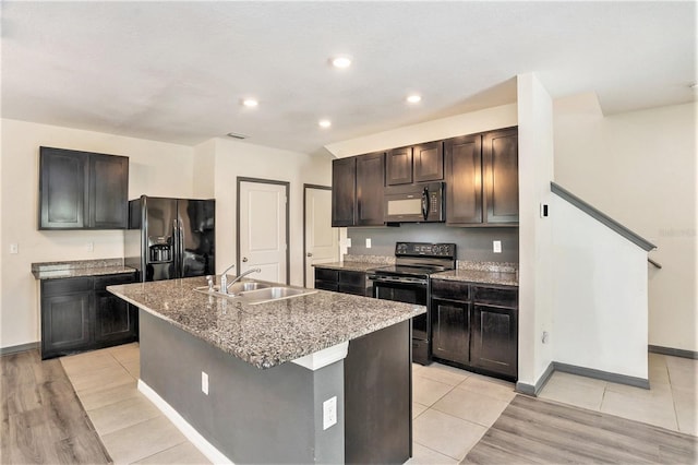 kitchen with a kitchen island with sink, light hardwood / wood-style flooring, black appliances, light stone counters, and sink