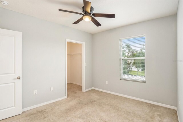 unfurnished bedroom featuring light colored carpet, ceiling fan, a spacious closet, and a closet