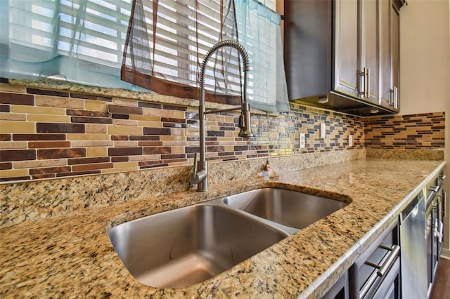 kitchen with stainless steel dishwasher, backsplash, sink, and light stone countertops