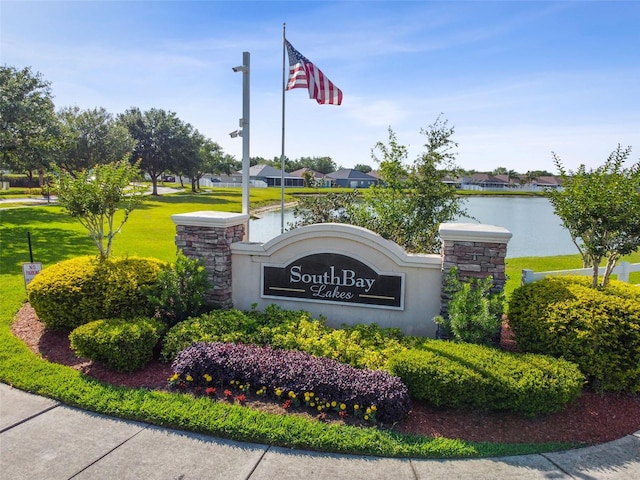 community / neighborhood sign featuring a water view and a yard