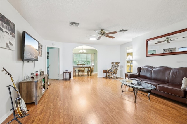 living area featuring ceiling fan with notable chandelier, visible vents, arched walkways, and light wood-style floors
