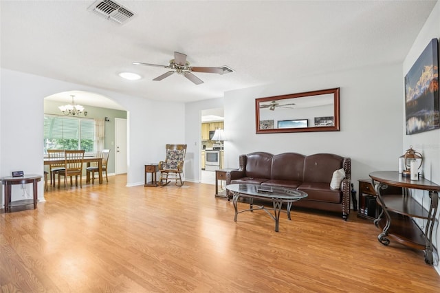 living room featuring light wood finished floors, baseboards, ceiling fan with notable chandelier, visible vents, and arched walkways