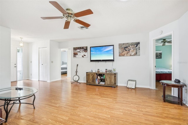 living area with baseboards, visible vents, light wood-style floors, ceiling fan, and a healthy amount of sunlight