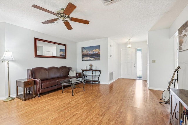 living room with ceiling fan, a textured ceiling, and light wood-type flooring