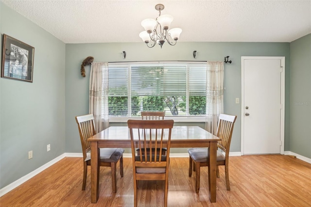 dining space with an inviting chandelier, light wood-style flooring, baseboards, and a textured ceiling