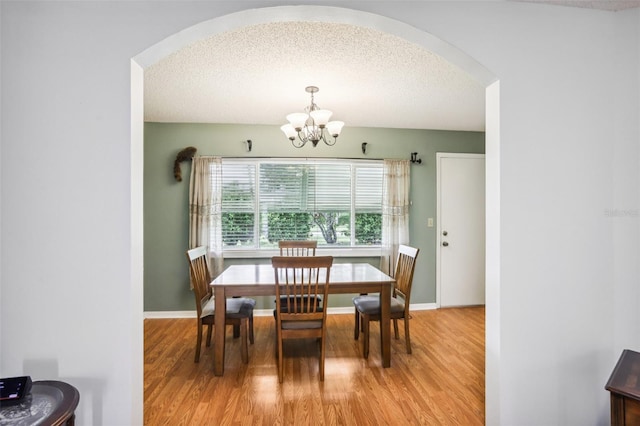 dining room featuring an inviting chandelier, baseboards, a textured ceiling, arched walkways, and light wood finished floors