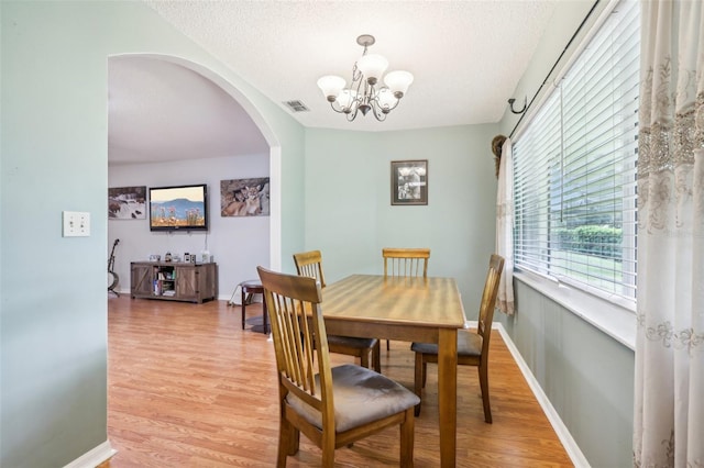 dining room featuring an inviting chandelier, light wood-style flooring, arched walkways, and a textured ceiling