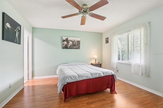 bedroom with a textured ceiling, baseboards, and wood finished floors