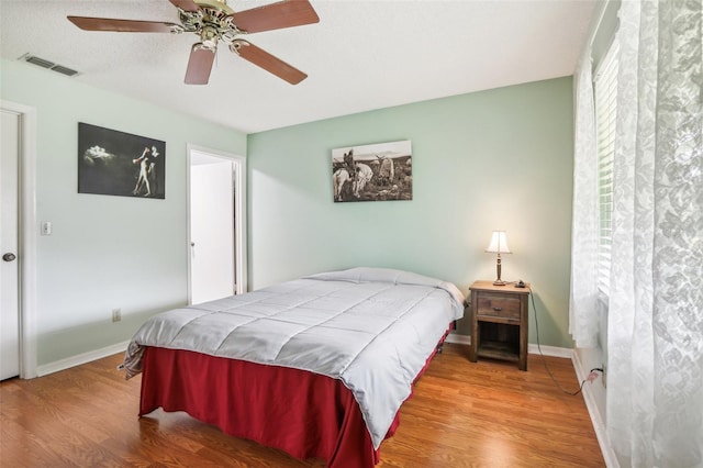 bedroom featuring baseboards, visible vents, wood finished floors, and a ceiling fan