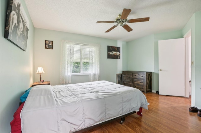 bedroom with a textured ceiling, wood-type flooring, and ceiling fan