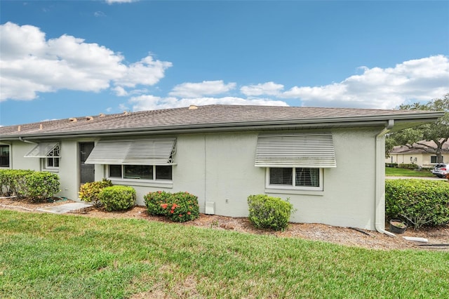 back of property featuring a lawn, roof with shingles, and stucco siding