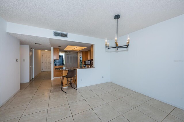 7037 Sunset Dr S Unit 602, South Pasadena, FL 33707 - kitchen with visible vents, a notable chandelier, dark countertops, a textured ceiling, and brown cabinets