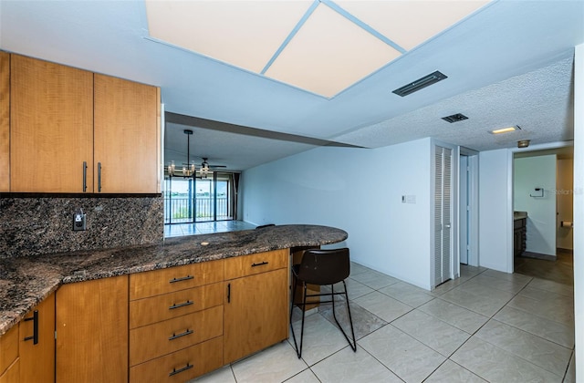 kitchen featuring a breakfast bar, kitchen peninsula, light tile patterned floors, and dark stone counters