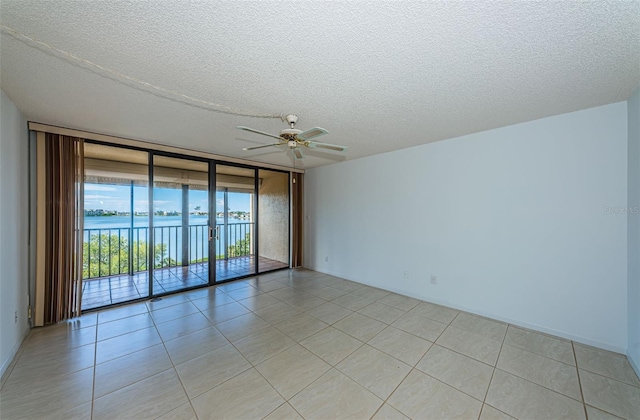 tiled empty room featuring ceiling fan, a textured ceiling, a wall of windows, and a water view