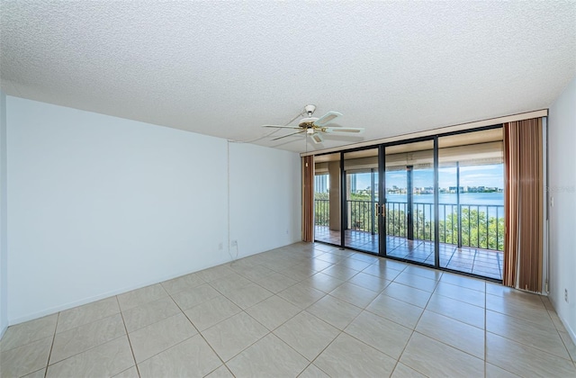 tiled spare room featuring a textured ceiling, a water view, ceiling fan, and expansive windows