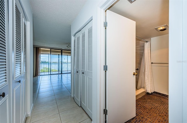 hall featuring a textured ceiling, floor to ceiling windows, and light tile patterned floors