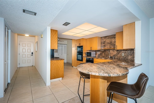 kitchen with light tile patterned floors, kitchen peninsula, tasteful backsplash, black appliances, and a kitchen bar