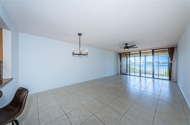 unfurnished room with ceiling fan with notable chandelier, a textured ceiling, a wall of windows, and light tile patterned flooring