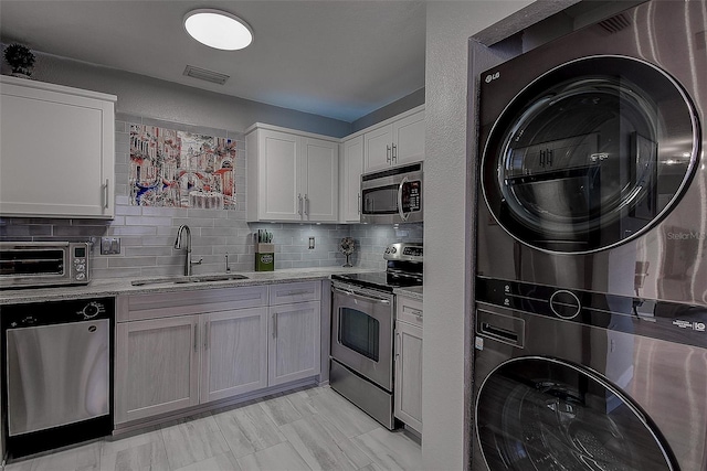 kitchen with stainless steel appliances, stacked washer and clothes dryer, white cabinetry, sink, and tasteful backsplash