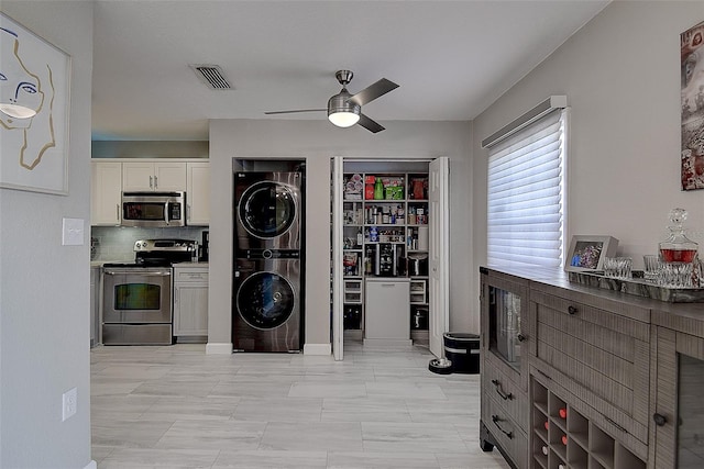 kitchen featuring appliances with stainless steel finishes, stacked washing maching and dryer, white cabinetry, ceiling fan, and tasteful backsplash