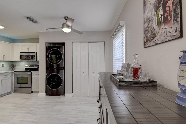 kitchen with appliances with stainless steel finishes, stacked washing maching and dryer, white cabinetry, ceiling fan, and tasteful backsplash