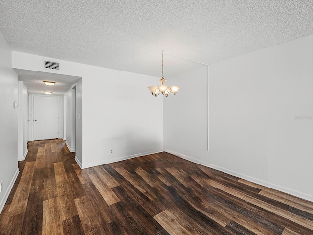 empty room with dark wood-type flooring, a textured ceiling, and a notable chandelier