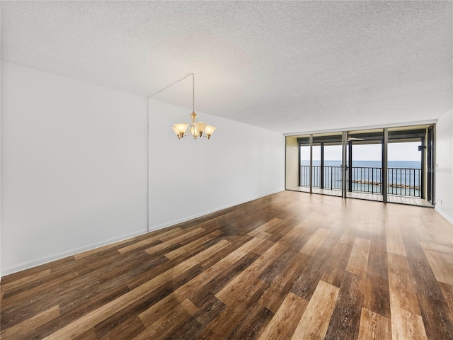 spare room with dark wood-type flooring, a chandelier, a textured ceiling, and a water view