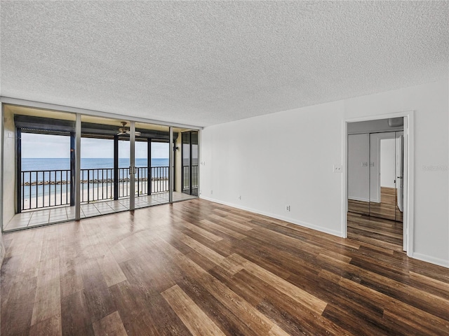 7100 Sunset Way Unit 405, St Pete Beach, FL 33706 - empty room featuring wood finished floors, a textured ceiling, a water view, baseboards, and floor to ceiling windows