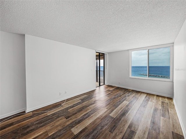 spare room with dark wood-type flooring, a water view, and a textured ceiling