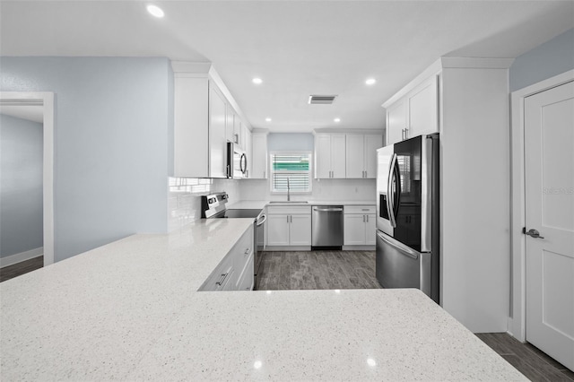 kitchen with appliances with stainless steel finishes, kitchen peninsula, white cabinetry, light stone counters, and dark hardwood / wood-style floors