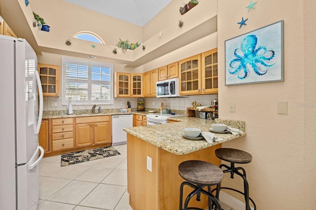 kitchen with white appliances, backsplash, kitchen peninsula, light stone countertops, and a breakfast bar