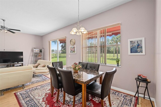 dining space with ceiling fan with notable chandelier and wood-type flooring