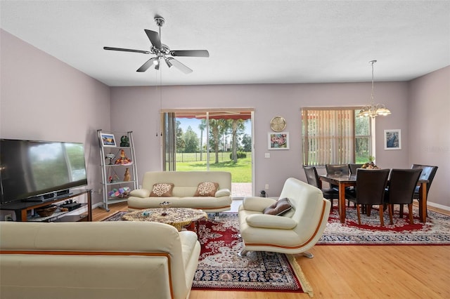 living room featuring wood-type flooring, plenty of natural light, ceiling fan with notable chandelier, and a textured ceiling