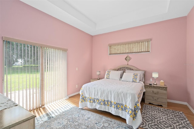 bedroom with access to exterior, light hardwood / wood-style floors, and a tray ceiling