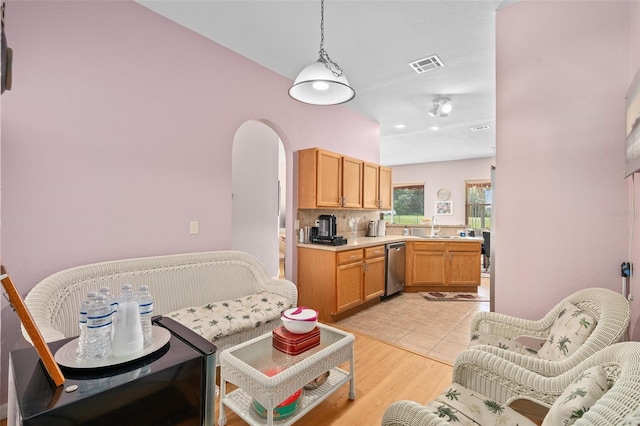 kitchen featuring light wood-type flooring, hanging light fixtures, stainless steel dishwasher, and tasteful backsplash