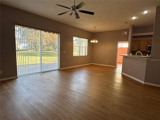 unfurnished living room with ceiling fan with notable chandelier and dark hardwood / wood-style flooring