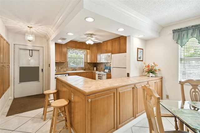 kitchen with light tile patterned floors, ceiling fan with notable chandelier, white appliances, sink, and a kitchen bar