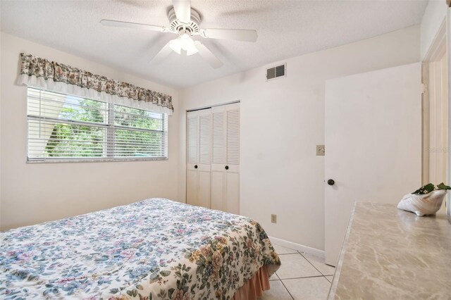 bedroom featuring a closet, light tile patterned floors, a ceiling fan, a textured ceiling, and baseboards