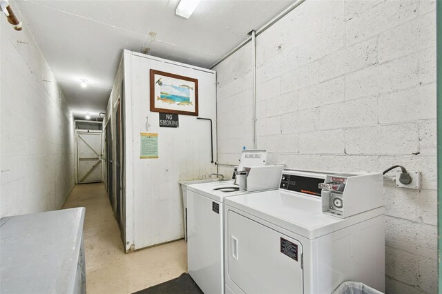 community laundry room with washing machine and clothes dryer and concrete block wall