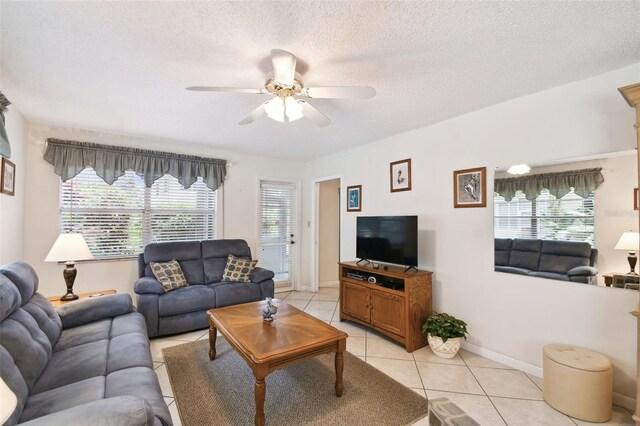 living area featuring a ceiling fan, light tile patterned floors, healthy amount of natural light, a textured ceiling, and baseboards