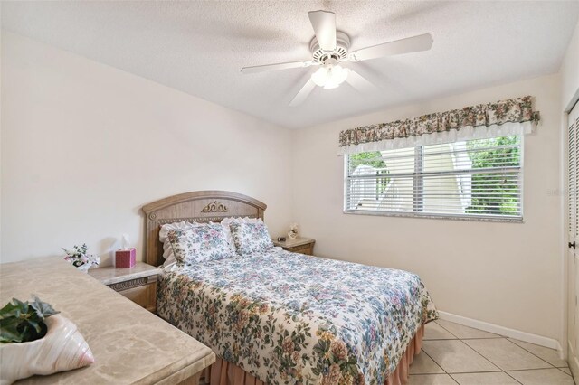 bedroom featuring light tile patterned floors, baseboards, a ceiling fan, a closet, and a textured ceiling