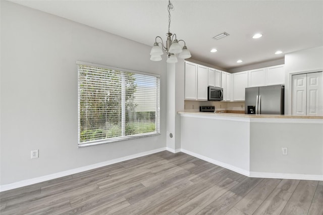 kitchen featuring light wood-type flooring, stainless steel appliances, pendant lighting, and white cabinets